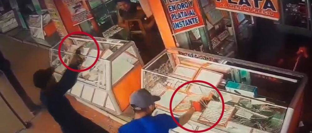 [Foto- captura video] : Uno de los sujetos amenaza a las víctimas mientras el otro saca las joyas
